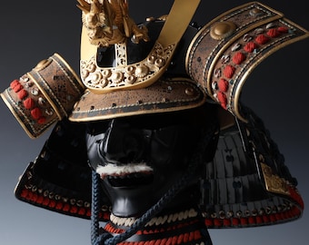 May include: A black samurai helmet with gold and red accents. The helmet has a detailed design with intricate patterns and a fierce expression.