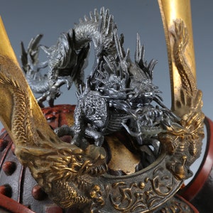 Puede incluir: Primer plano de un casco de samur&aacute;i japon&eacute;s. El casco presenta una pieza central de drag&oacute;n plateado detallada y detalles dorados. El dise&ntilde;o del casco incluye elementos lacados en rojo y negro, mostrando una artesan&iacute;a intrincada.
