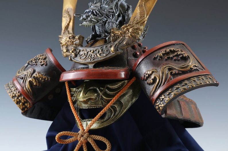 Puede incluir: Primer plano de un casco de samur&aacute;i japon&eacute;s. El casco presenta una cresta de drag&oacute;n, intrincados detalles dorados y una combinaci&oacute;n de colores rojo y negro. Los protectores de hombro tienen un dise&ntilde;o de olas.