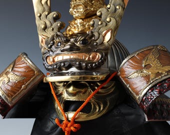May include: A samurai helmet with a gold and black lion design, a red and gold eagle design on the shoulder pads, and a red rope tied around the helmet.
