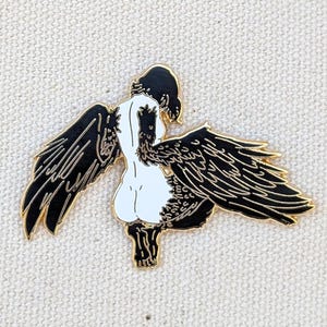 Harpy mythical creature enamel pin detailed wings gold enamel displayed against textured canvas