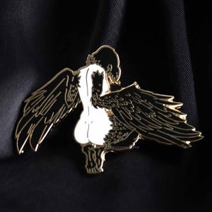 Close up of black haired Harpy mythical creature with black and gold enamel pin detailed wings with a black satin background.