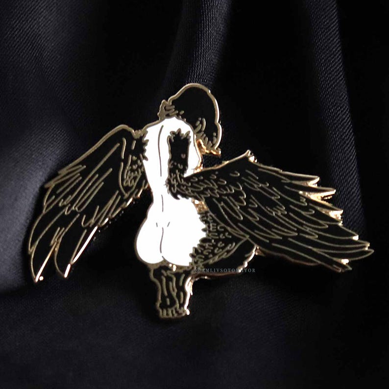 Close up of black haired Harpy mythical creature with black and gold enamel pin detailed wings with a black satin background.