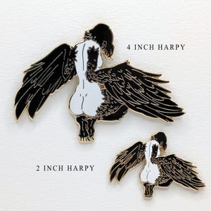 Two different sized enamel pins showing a large 4 inch of black haired Harpy mythical creature with a 2" inch black haired Harpy mythical creature. Both harpies are gold enamel pins with black wings and an exposed buttocks.