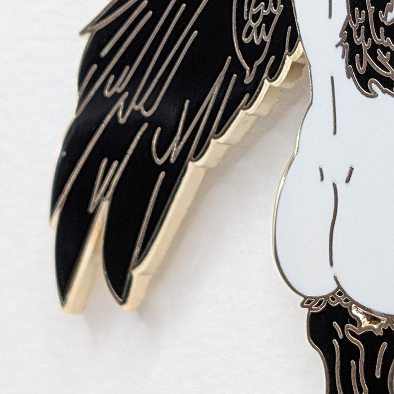 Close up showing detail of black Harpy mythical creature with black and gold enamel pin detailed wings and the butt.