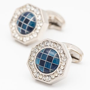 May include: A pair of silver cufflinks with a blue and black checkered design surrounded by clear rhinestones.