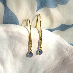 May include: A pair of gold dangle earrings with blue teardrop-shaped stones. The earrings have a textured gold finish.