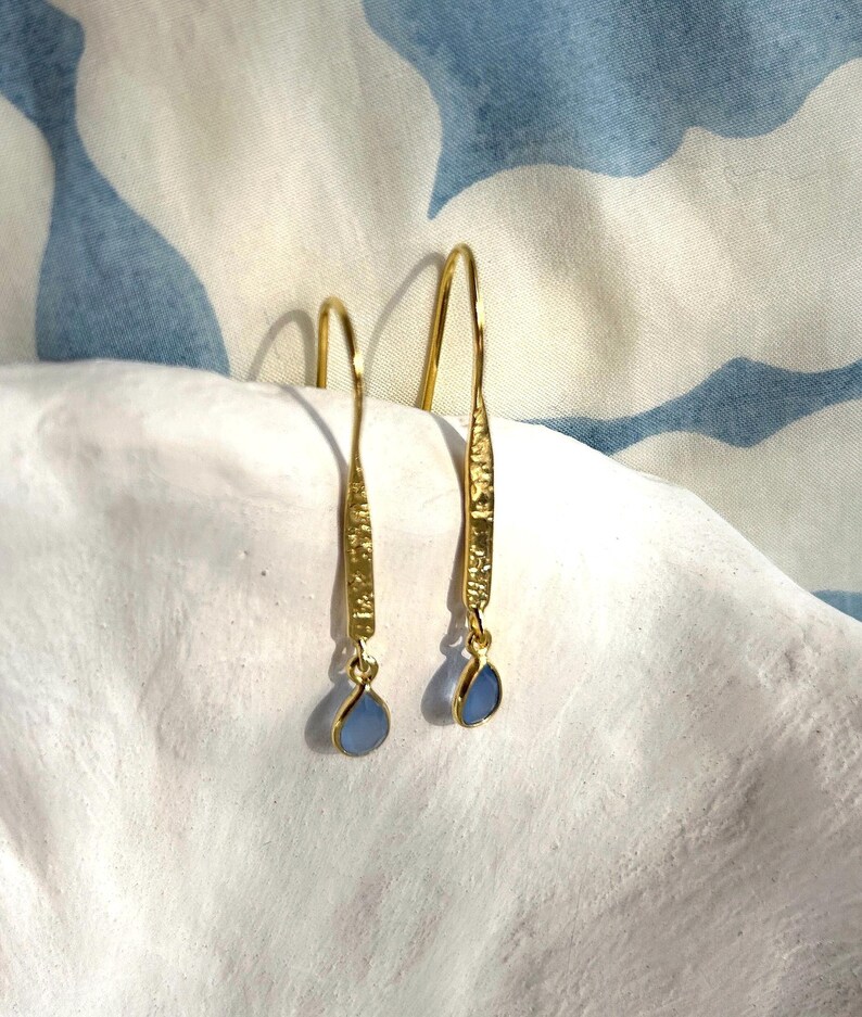 May include: A pair of gold dangle earrings with blue teardrop-shaped stones. The earrings have a textured gold finish.