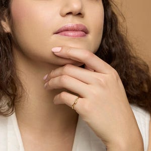 Puede incluir: Un anillo de oro con un dise&ntilde;o delicado en forma de hoja. El anillo se lleva en un dedo. La imagen es un primer plano, que muestra los detalles del anillo. El anillo es una joya. Se ve el tono de piel de la persona que lo lleva.