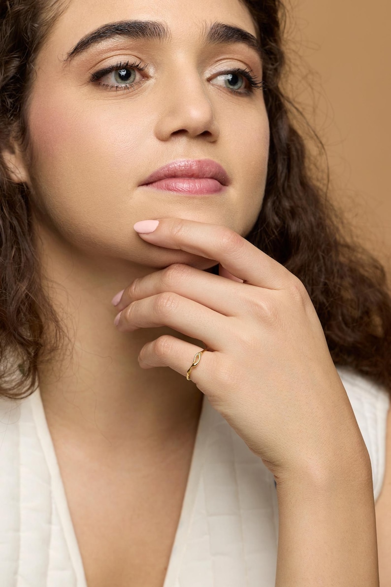 Puede incluir: Un anillo de oro con un dise&ntilde;o delicado en forma de hoja. El anillo se lleva en un dedo. La imagen es un primer plano, que muestra los detalles del anillo. El anillo es una joya. Se ve el tono de piel de la persona que lo lleva.