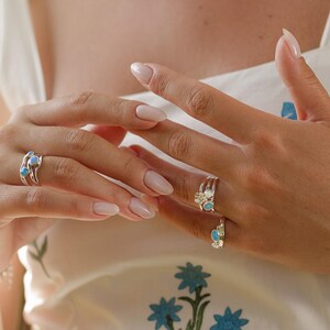 May include: Silver rings with blue gemstone accents are displayed on a hand. The rings have a delicate, nature-inspired design. One ring features a cluster of three gemstones, while the others have a single gemstone.