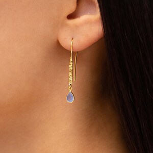 May include: Gold dangle earrings with a light blue teardrop-shaped gemstone.