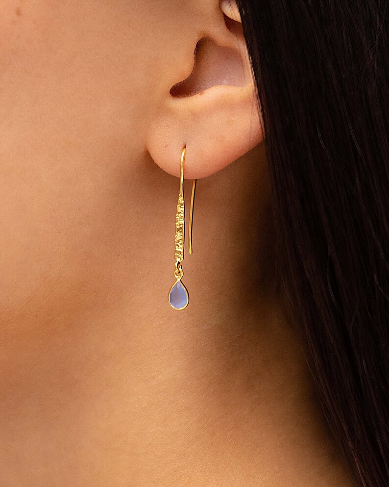 May include: Gold dangle earrings with a light blue teardrop-shaped gemstone.