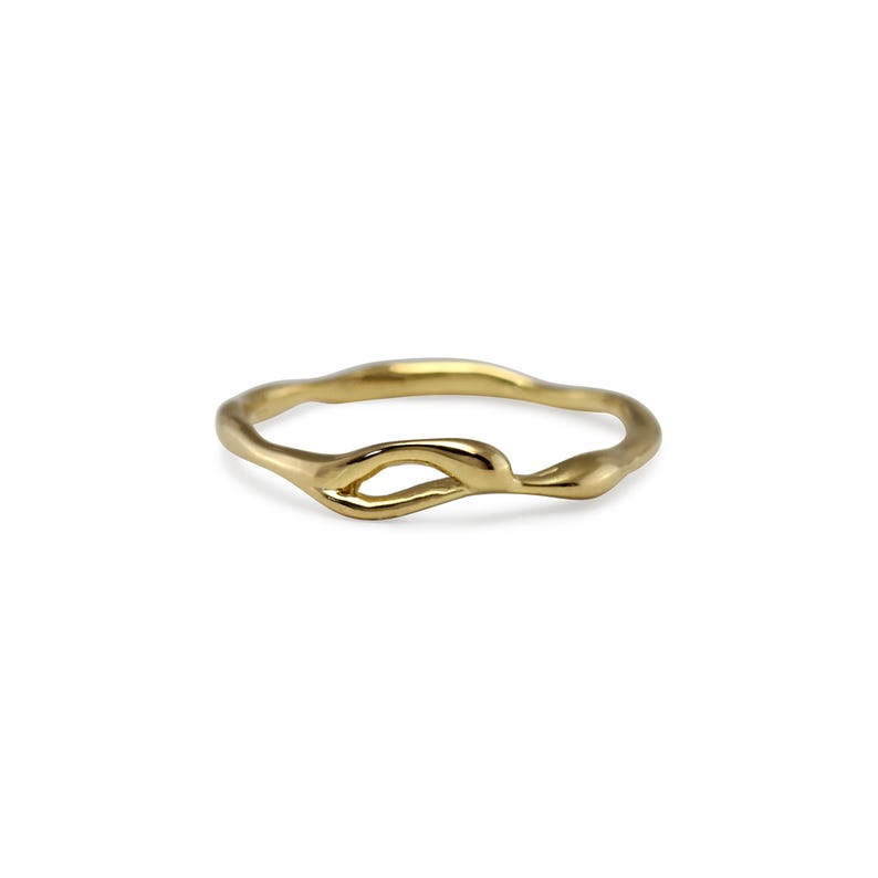 Puede incluir: Un anillo dorado con un dise&ntilde;o org&aacute;nico y fluido. El anillo presenta un detalle en forma de nudo en el centro, con un acabado liso y pulido. El anillo se muestra sobre un fondo blanco, resaltando su forma y color.