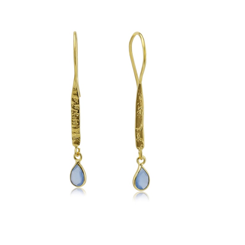 May include: A pair of gold drop earrings with a light blue teardrop-shaped gemstone hanging from each earring.