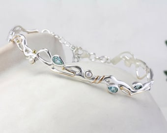 May include: A silver and gold bracelet with a delicate, organic design. The bracelet features blue gemstones and a pearl.