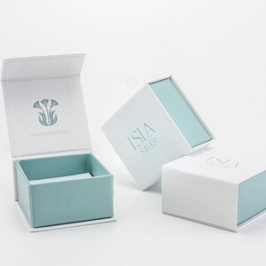 May include: Three white gift boxes with blue lids. The boxes are labeled "Isla Silver" and feature a floral design.