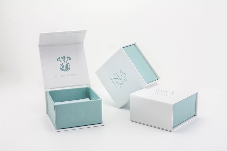 May include: Three white gift boxes with blue lids. The boxes are labeled "Isla Silver" and feature a floral design.