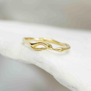 Puede incluir: Un delicado anillo de oro con un dise&ntilde;o org&aacute;nico y fluido. El anillo presenta un detalle &uacute;nico de centro abierto y un acabado liso y pulido. El anillo se encuentra sobre un fondo blanco suave, resaltando su elegante forma. Ideal para el uso diario.