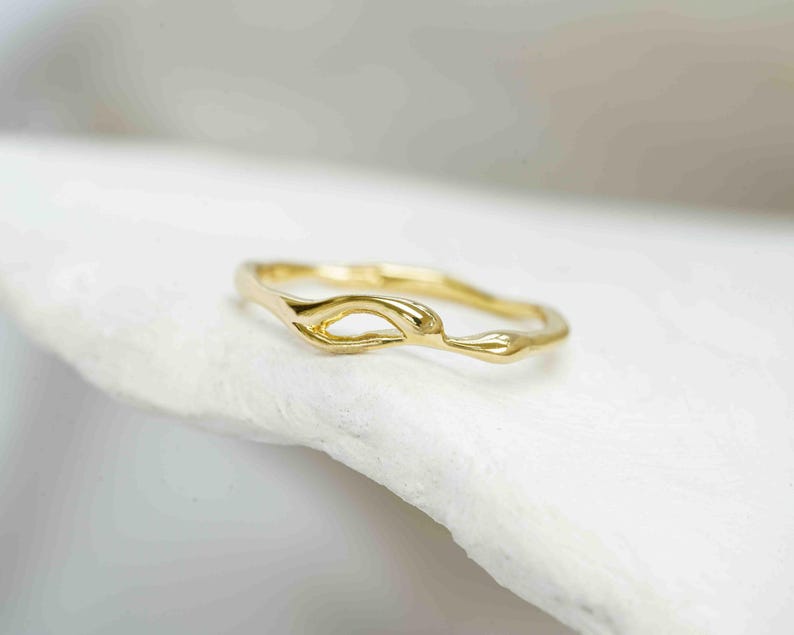 Puede incluir: Un delicado anillo de oro con un dise&ntilde;o org&aacute;nico y fluido. El anillo presenta un detalle &uacute;nico de centro abierto y un acabado liso y pulido. El anillo se encuentra sobre un fondo blanco suave, resaltando su elegante forma. Ideal para el uso diario.