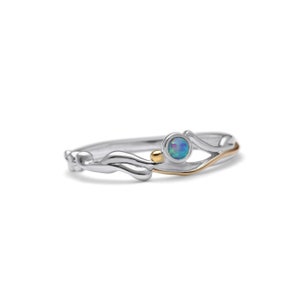 May include: A silver ring with a gold accent and a round, blue-green opal stone. The ring has a delicate, flowing design with a small gold bead. The opal stone is set in a silver bezel.