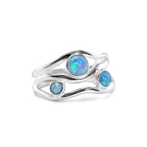May include: A set of three silver rings with a flowing, organic design. Each ring features a round, iridescent blue opal stone. The rings are stacked together, creating a unique and eye-catching jewelry piece.