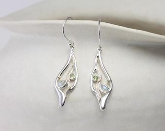 May include: A pair of silver drop earrings featuring a fluid, open-work design. Each earring is accented with a small, round, light green gemstone and a teardrop-shaped, iridescent white stone, suspended from a simple silver hook wire.