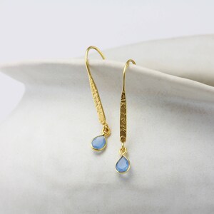 May include: A pair of gold dangle earrings with light blue teardrop-shaped gemstones.