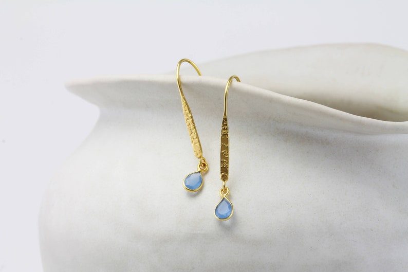 May include: A pair of gold dangle earrings with light blue teardrop-shaped gemstones.