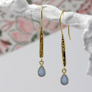 May include: Gold dangle earrings with a textured bar and a light blue teardrop-shaped gemstone.