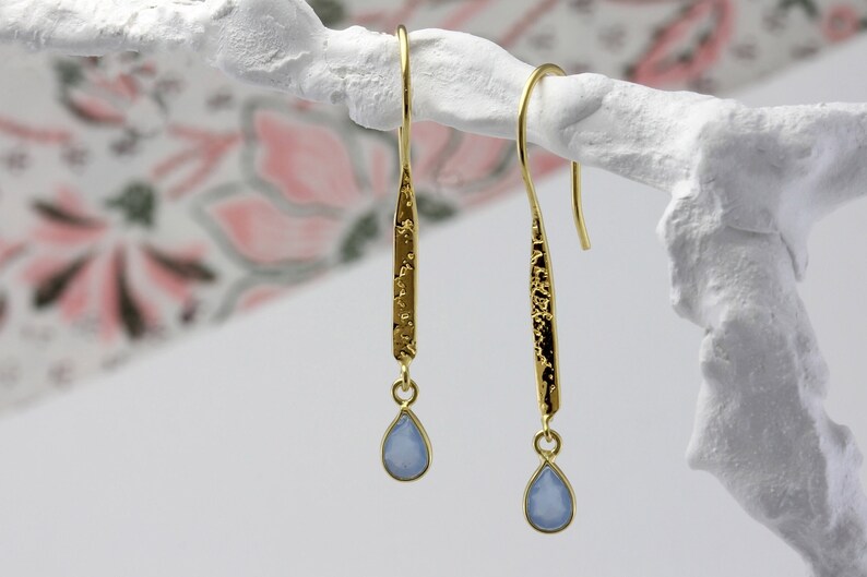 May include: Gold dangle earrings with a textured bar and a light blue teardrop-shaped gemstone.
