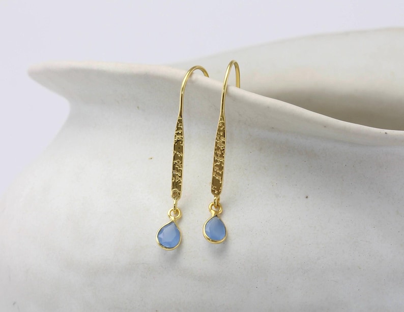 May include: A pair of gold dangle earrings with light blue teardrop-shaped stones.