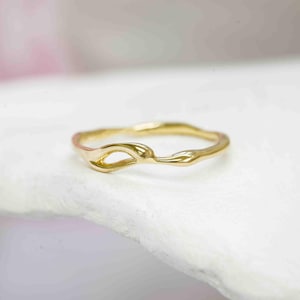 Puede incluir: Un delicado anillo de oro con un dise&ntilde;o org&aacute;nico y fluido. El anillo presenta una forma &uacute;nica con una abertura central y una superficie texturizada. El color dorado c&aacute;lido del anillo contrasta con el fondo blanco.