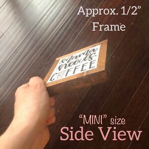 May include: Side view of a small wooden sign with the text "Mama needs coffee" in black lettering. The sign is approximately 1/2 inch thick and is held in a hand. The sign is labeled "MINI" size.