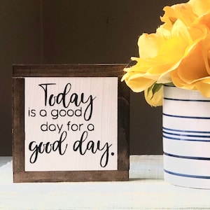 Peut inclure: Panneau en bois avec l'inscription "Today is a good day for a good day" en &eacute;criture noire. Le panneau est encadr&eacute; de bois brun fonc&eacute;. Des fleurs jaunes sont dans un vase blanc &agrave; rayures bleues.