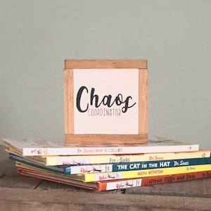K&ouml;nnte beinhalten: Eine Holzkiste mit dem Text "Chaos Coordinator" auf wei&szlig;em Hintergrund. Die Kiste steht auf einem Stapel Dr. Seuss-B&uuml;cher, darunter "Der Kater mit Hut", "Gr&uuml;n, gr&uuml;n, gr&uuml;n sind alle meine Eier" und "Der Fuchs in Socken".