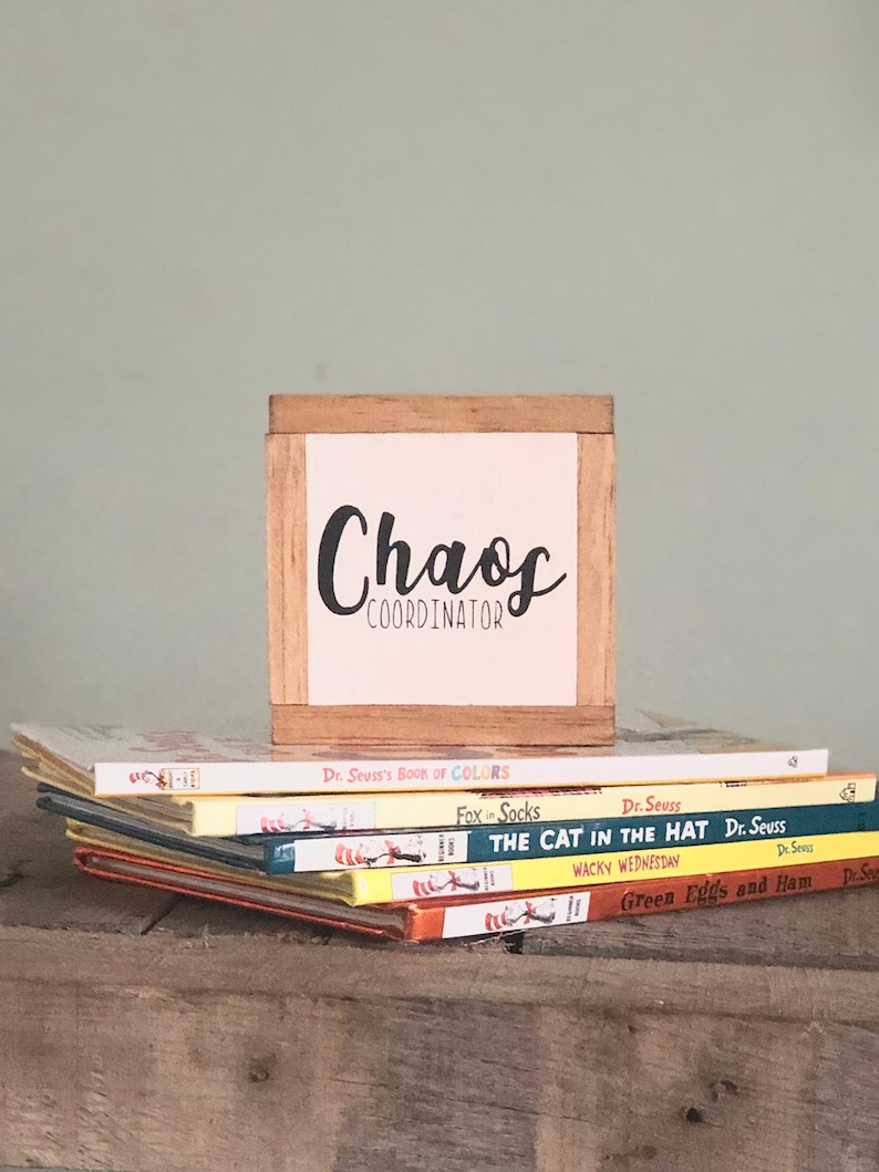 K&ouml;nnte beinhalten: Eine Holzkiste mit dem Text "Chaos Coordinator" auf wei&szlig;em Hintergrund. Die Kiste steht auf einem Stapel Dr. Seuss-B&uuml;cher, darunter "Der Kater mit Hut", "Gr&uuml;n, gr&uuml;n, gr&uuml;n sind alle meine Eier" und "Der Fuchs in Socken".