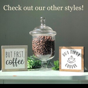 May include: Two wooden signs with the text "But First, Coffee" in black lettering. One sign has a coffee cup icon. A glass jar filled with coffee beans sits between the signs.