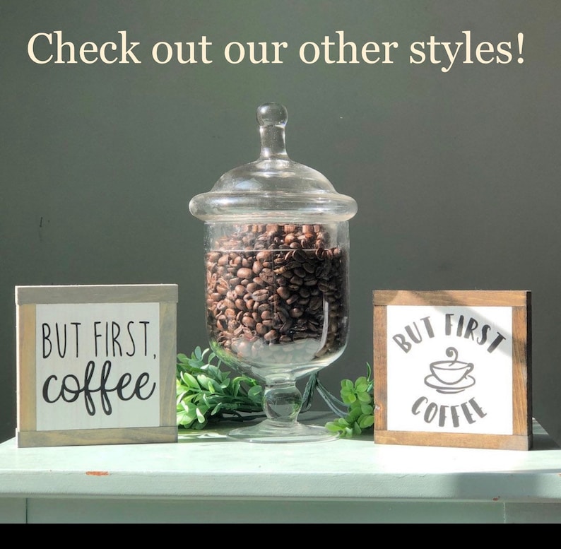 May include: Two wooden signs with the text "But First, Coffee" in black lettering. One sign has a coffee cup icon. A glass jar filled with coffee beans sits between the signs.