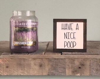 May include: A Yankee Candle lavender-scented candle in a glass jar, next to a small wooden sign that reads "Have a Nice Poop". The candle has a label with a lavender field image. The candle weighs 22 oz.