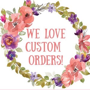 May include: A floral wreath with pink and purple flowers surrounds the text "WE LOVE CUSTOM ORDERS!" on a white background.