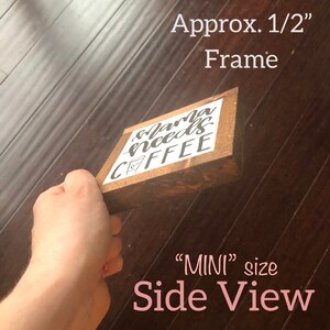 Puede incluir: Vista lateral de un peque&ntilde;o letrero de madera con el texto "Mama needs coffee" en letras negras sobre fondo blanco. El letrero tiene aproximadamente 1,27 cm de grosor y est&aacute; enmarcado en madera. El letrero se sostiene en una mano.