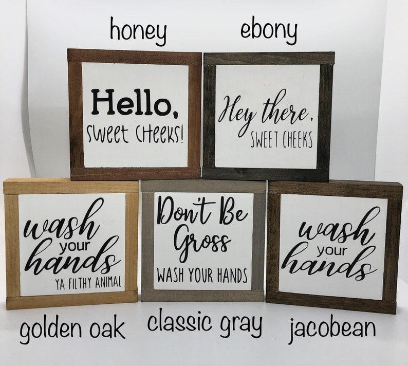 May include: Four wooden signs with different sayings and wood stains. The signs read "Hello, Sweet Cheeks!" in honey stain, "Hey there, Sweet Cheeks" in ebony stain, "Wash your hands, Ya Filthy Animal" in golden oak stain, and "Don't Be Gross, Wash Your Hands" in classic gray stain. The signs are all the same size and shape.