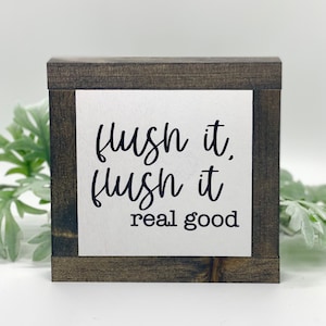 May include: A small wooden sign with a white background and black text that reads "flush it, flush it real good".