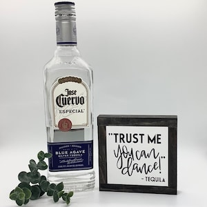Puede incluir: Un letrero de madera con texto negro que dice "TRUST ME you can dance! - TEQUILA" est&aacute; al lado de una botella de tequila Jose Cuervo Especial Blue Agave Silver.