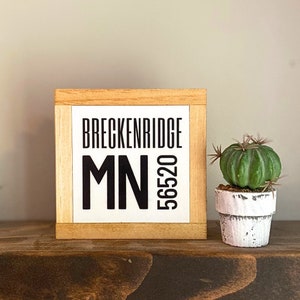 May include: A wooden sign with the text "Breckenridge MN 56520" in black lettering on a white background.