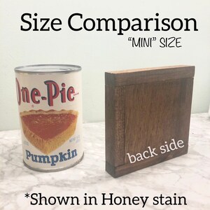 May include: Size comparison of a wooden sign with the text "back side" and a can of pumpkin pie filling. The sign is stained in a honey color. The text "MINI" SIZE is written above the sign. The text "*Shown in Honey stain" is written below the sign.