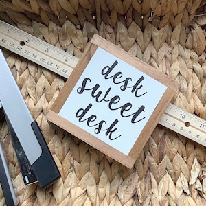 Op de afbeelding: Een houten bord met een witte achtergrond en zwarte letters met de tekst "desk sweet desk".
