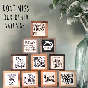 May include: A collection of nine wooden signs with coffee-themed sayings. The signs are stacked in a pyramid shape and feature phrases like "Mama needs coffee", "Rise and Grind", "Stressed Blessed and Coffee Obsessed", and "Life Begins After Coffee!"
