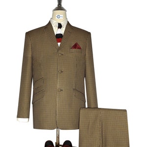Può includere: Una giacca e pantaloni da abito a pied-de-poule marrone e nero con una camicia bianca e una cravatta a righe rosse e nere. Il vestito è su un manichino e ci sono mocassini in pelle marrone con nappine in primo piano.